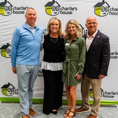 Two men and two women posing together at the Charlie's House backdrop
