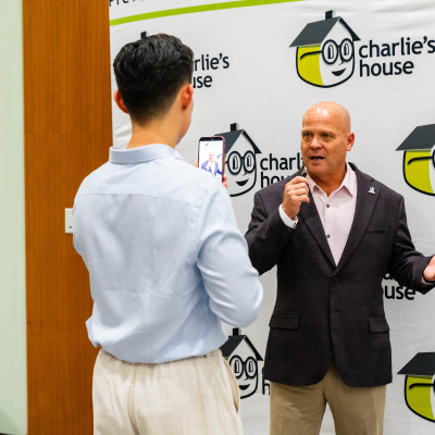 Man in a dark blazer speaking to a phone camera held by a guest at the Charlie's House backdrop