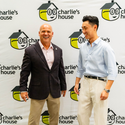 Two men laughing together in front of the Charlie's House banner