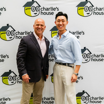Two men posing for a full-length photo at the Charlie's House backdrop