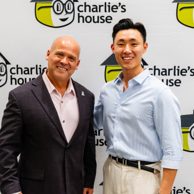 Two men smiling side by side in front of the Charlie's House logo wall