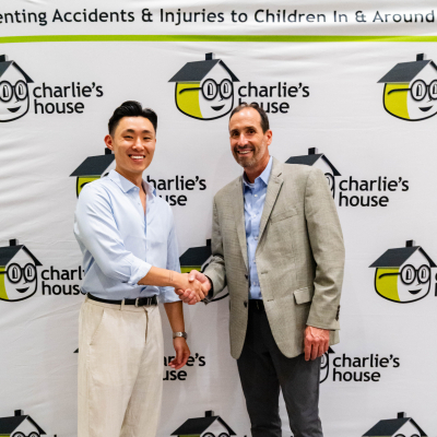 Two men shaking hands in front of the Charlie's House backdrop