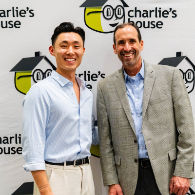 Two men smiling in front of the Charlie's House logo backdrop