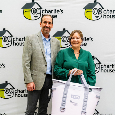 Man and woman holding a white YETI cooler bag in front of the Charlie's House backdrop