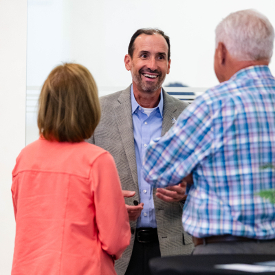 Man in a tweed blazer laughing with two guests at the reception