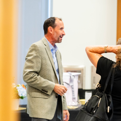 Man in a tan blazer smiling while chatting with a guest at the reception