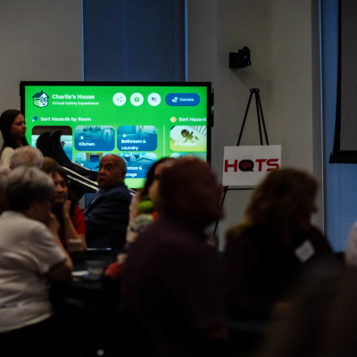 Guests seated at tables watching a presentation of the Charlie's House website on a screen