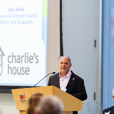 Speaker smiling at the podium in front of a Charlie's House slide as guests listen