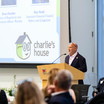 Speaker at a podium addressing the audience in front of a Charlie's House presentation screen