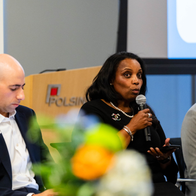 Panelist in a black dress with pearls speaking into a microphone