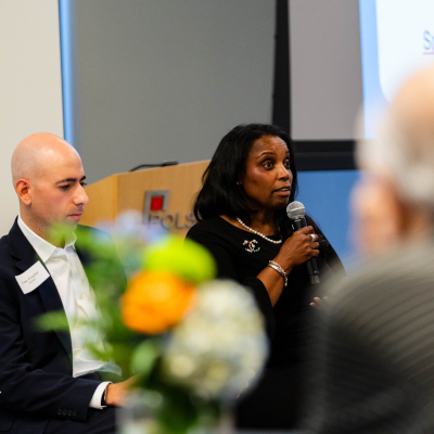 Panelist in a black dress speaking into a microphone beside a fellow panelist