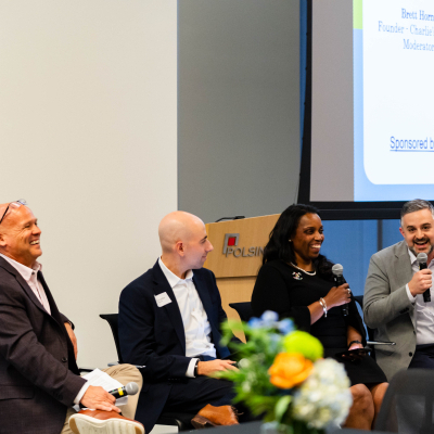 Panelist in a gray blazer speaking and gesturing while the rest of the panel smiles