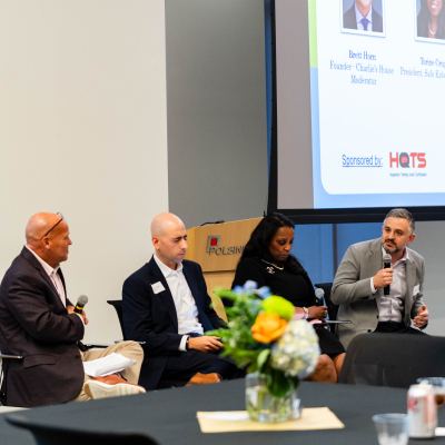 Four panelists seated in front of a screen titled How Education, with a floral centerpiece on the table