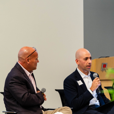 Two panelists seated side by side, one speaking into a microphone