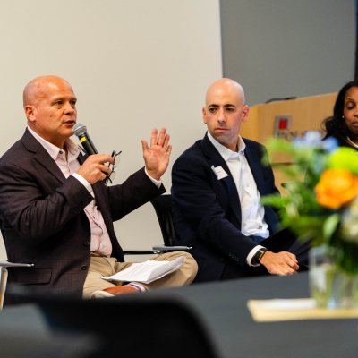 Panelist gesturing while speaking into a microphone as fellow panelists listen