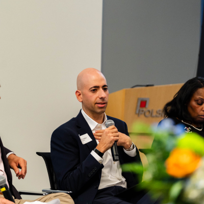 Panelist in a navy suit speaking into a microphone, with flowers on the table in front