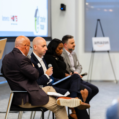 Wide view of the four-person panel seated beside a Charlie's House presentation screen