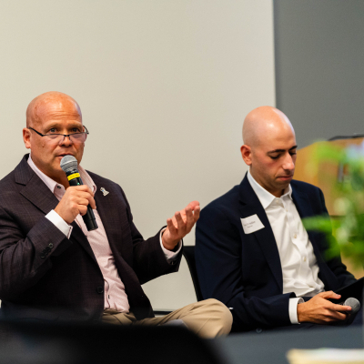 Panelist in a dark blazer speaking into a microphone beside a fellow panelist