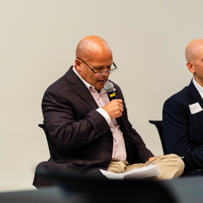 Seated panelist reading notes while speaking into a microphone