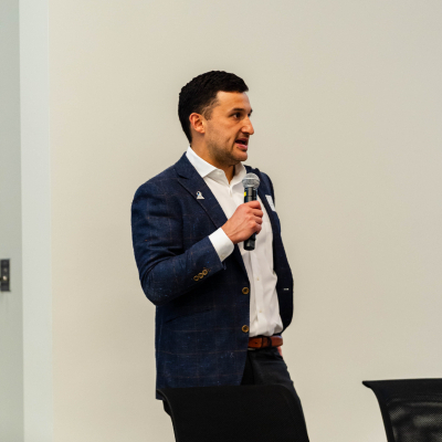 Man in a navy blazer standing and speaking to the audience with a microphone