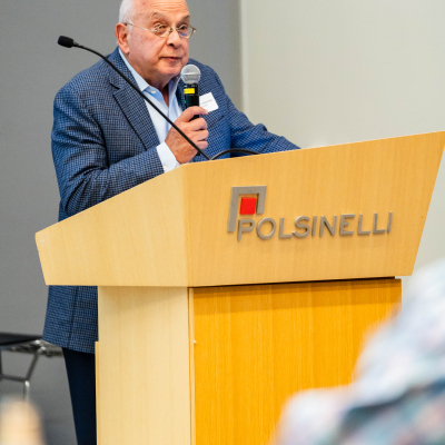 Speaker holding a microphone at the Polsinelli podium during the program