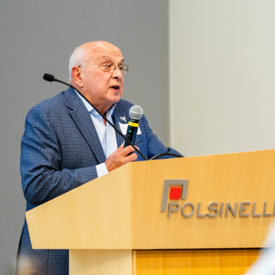 Older man in a blue blazer speaking into a microphone at the Polsinelli podium