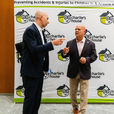 Two men talking and pointing in front of the Charlie's House banner