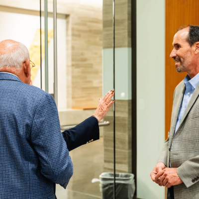 Older man gesturing while talking with a man in a tweed blazer