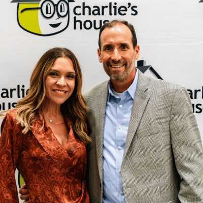 Man and woman smiling together in front of the Charlie's House backdrop