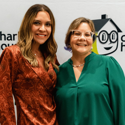 Two women smiling close together in front of the Charlie's House logo wall