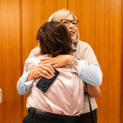 Two women sharing a warm hug against a wood-paneled wall