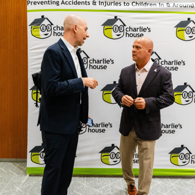 Two men in conversation in front of the Charlie's House Preventing Accidents & Injuries banner